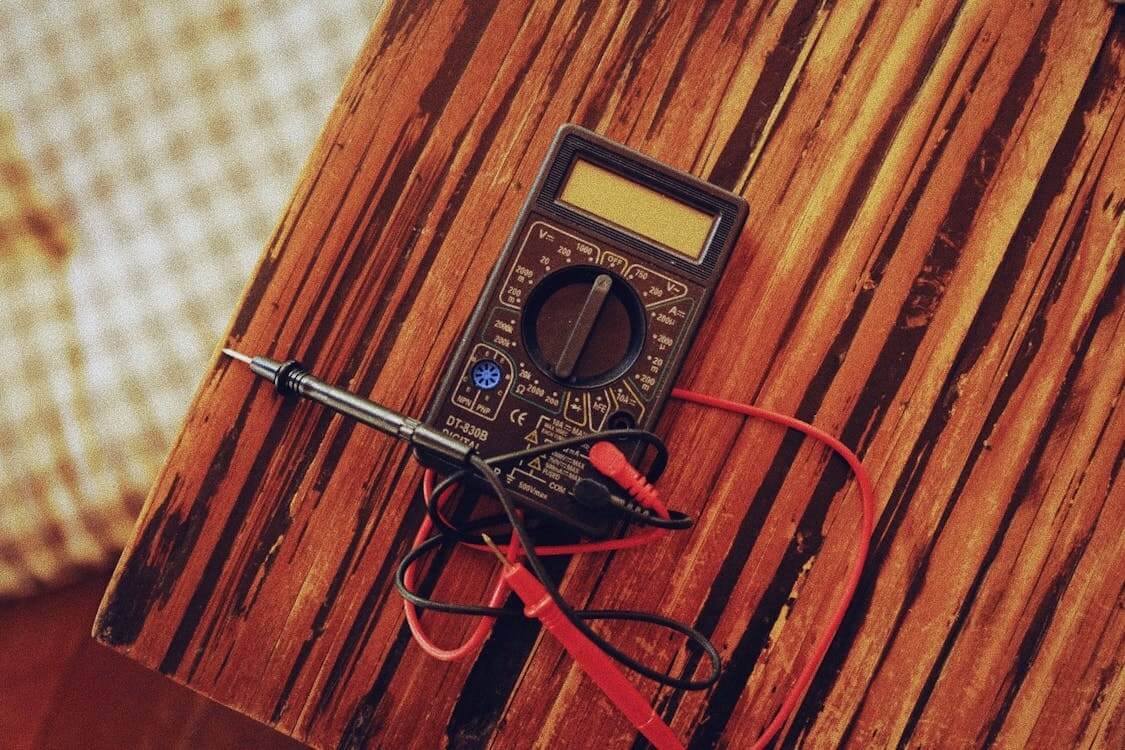 A multimeter with red and black probes lies on a wooden table