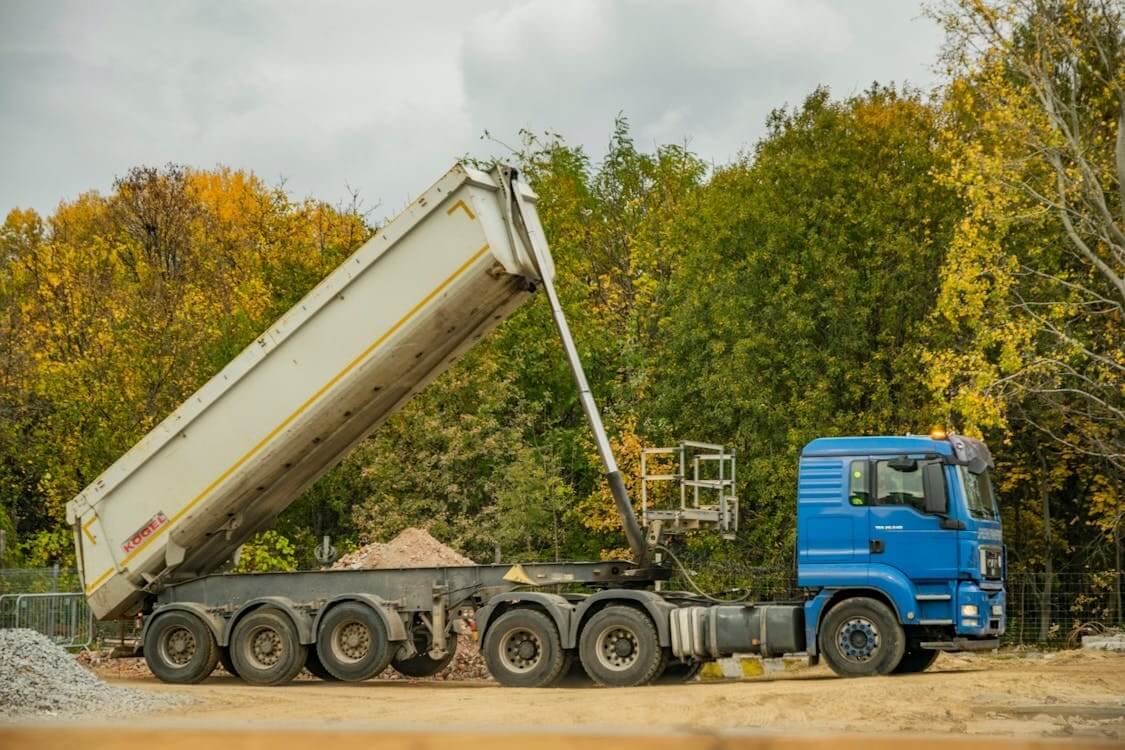 A tilt trailer is safely unloading sand at a construction site