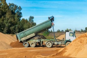 A tilt trailer is safely unloading sand at a construction site