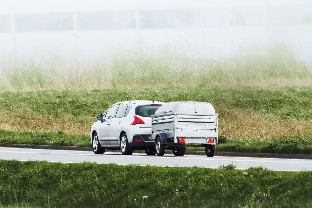 A white SUV drives down a highway on a foggy day, towing a small, open utility trailer