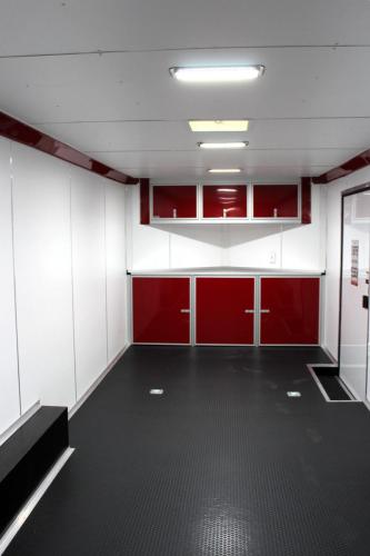 The front interior of this 24ft. aluminum car hauler features coin flooring, white walls  ceiling, red base & overhead cabinets, & d-rings.